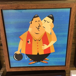 May include: Framed print featuring a stylized illustration of two figures embracing. One figure is kissing the other on the cheek. The figures are wearing bowling shirts and the background is blue. A bowling ball is in the foreground.
