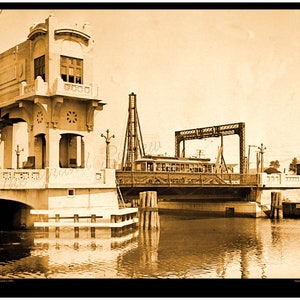 May include: A vintage black and white photograph of a drawbridge over a canal. The bridge is raised, allowing a streetcar to pass through. The bridge is made of metal and has a wooden deck. The streetcar is a vintage model with wooden seats and windows. The photograph is taken from a low angle, looking up at the bridge.