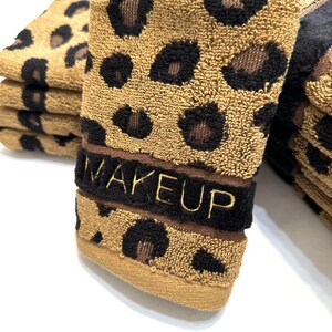 May include: A stack of brown and black leopard print hand towels with the word "MAKEUP" embroidered in gold on the top towel.