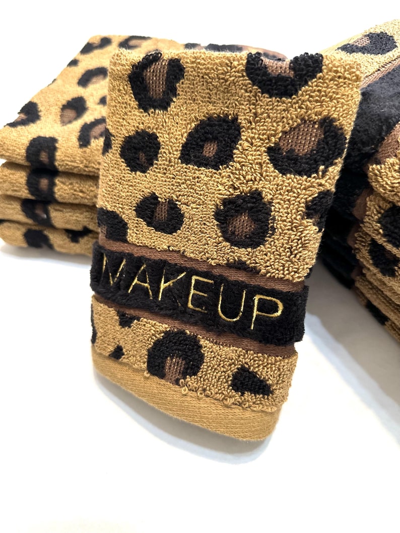 May include: A stack of brown and black leopard print hand towels with the word "MAKEUP" embroidered in gold on the top towel.