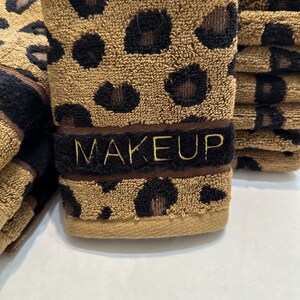 May include: A stack of brown and black leopard print towels with the word "MAKEUP" embroidered in gold on the front towel.