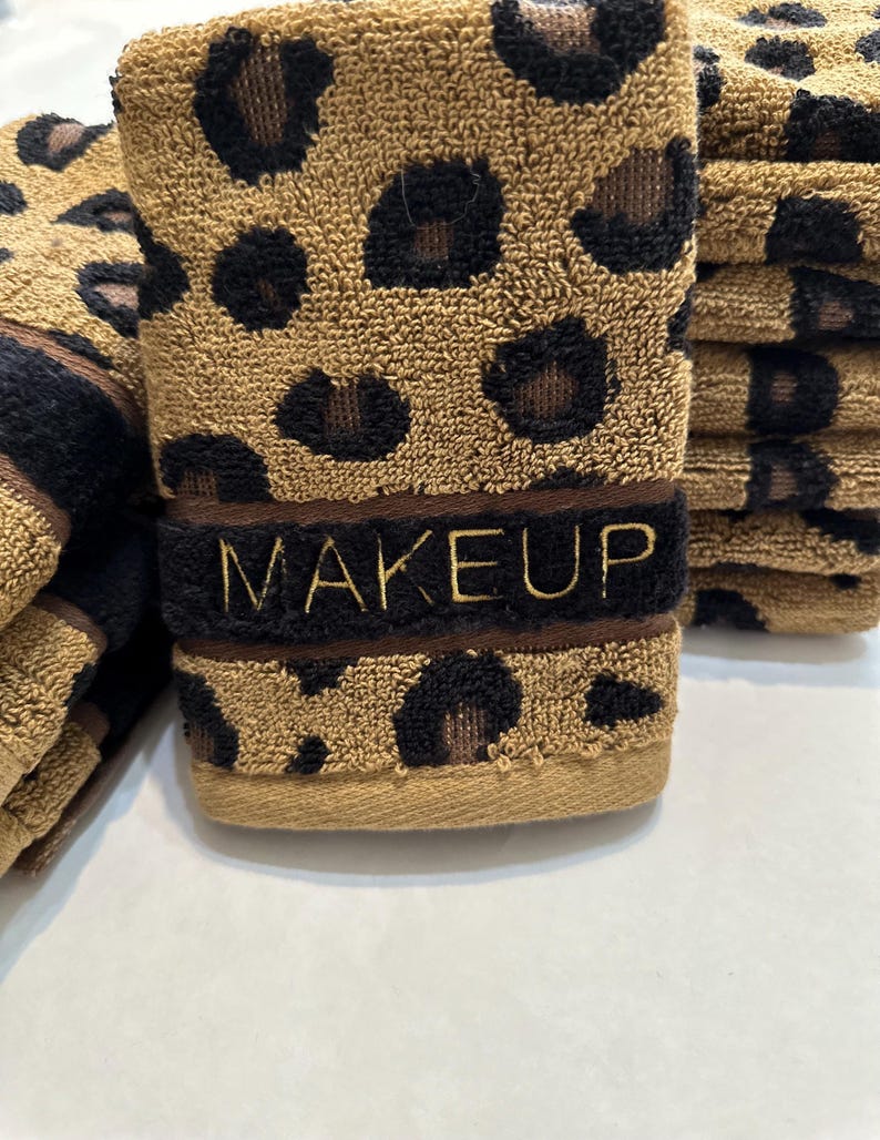May include: A stack of brown and black leopard print towels with the word "MAKEUP" embroidered in gold on the front towel.