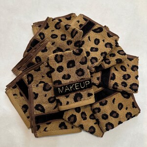 May include: A stack of brown and black leopard print makeup remover cloths with the word "MAKEUP" embroidered in gold on one of the cloths.