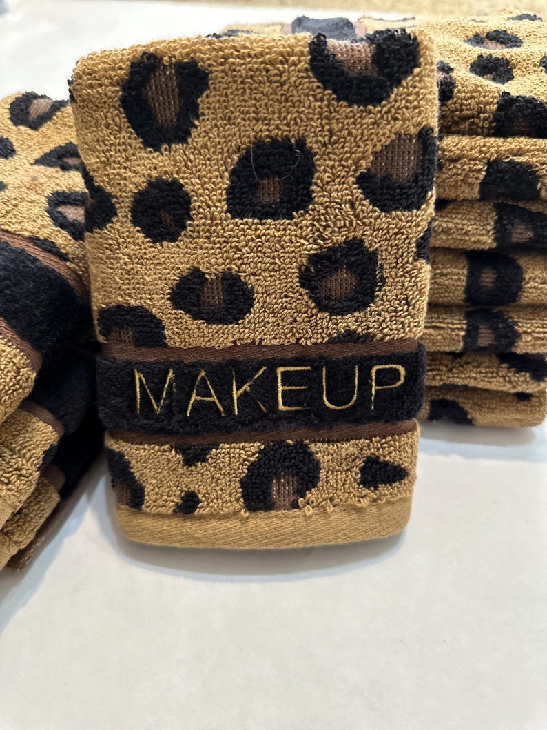 May include: A stack of brown and black leopard print hand towels with the word "MAKEUP" embroidered in gold on the front towel.