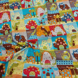 Könnte beinhalten: Ein farbenfroher Stoff mit einem sich wiederholenden Muster aus Comic-Dinosauriern. Die Dinosaurier sind in verschiedenen Farben, darunter Rot, Blau, Grün, Gelb und Braun. Der Stoff hat einen hellblauen Hintergrund mit einem Patchwork-Design. Der Stoff zeigt den Text "Dino Land", "Dinosaur", "Munch Munch", "Big Scary Teeth" und "Pipe His Own".