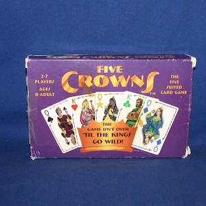 May include: A purple Five Crowns card game box with gold lettering and card illustrations. The box reads "Five Crowns" and "The Five Suited Card Game". The game is for 2-7 players, ages 8-adult. The text "The game isn't over 'til the kings go wild!" is also visible.