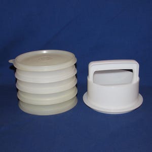 May include: A stack of off-white plastic lids and a white plastic container with a handle. The lids are round and have a slightly raised center. The container is cylindrical with a flat base and a handle.