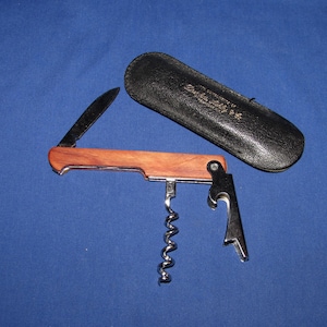 May include: A wooden handled multi-tool with a corkscrew, bottle opener, and a small knife. The tool is in a black leather case.