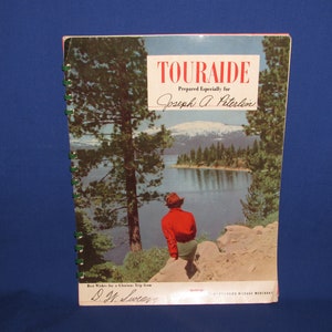 May include: A vintage book with a spiral binding featuring a scenic image of a lake with a mountain in the background. The book cover has the text "Touraide" and "Prepared Especially for Joseph A. Peterlin". The bottom of the cover has the text "Best Wishes for a Glorious Trip from D.H. Lucas".