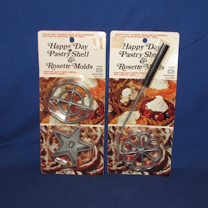 May include: Two vintage packages of Happy Day Pastry Shell & Rosette Molds. One package includes a star-shaped mold and a circular mold. The other package includes a rosette mold with a black handle. The packages have text and images of pastries.
