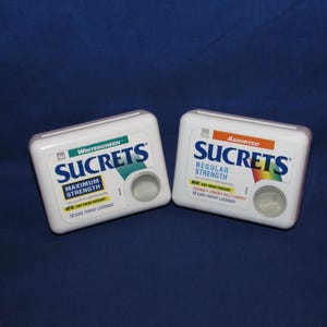 May include: Two white rectangular boxes of Sucrets throat lozenges. One box is labeled "Wintergreen Maximum Strength" and the other is "Assorted Regular Strength". Both boxes have a circular opening.