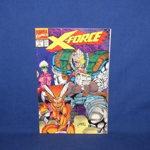 May include: X-Force comic book cover featuring a group of illustrated characters. The title "X-FORCE" is in large yellow and red letters. The cover art includes a cyborg-like figure with a gun, and other characters in action poses.