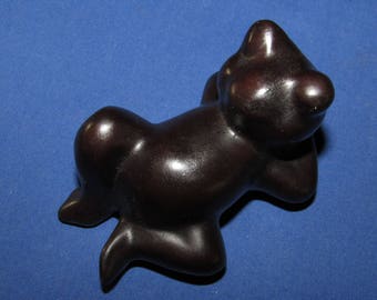 May include: A dark brown ceramic figurine of a stylized animal, possibly a dog or a cat, lying on its side with its head resting on its paw.