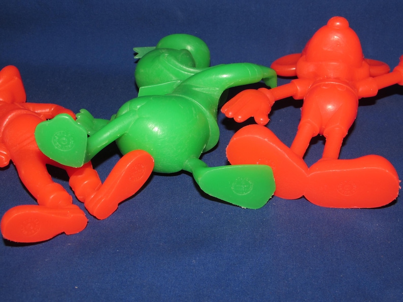 May include: Three plastic cartoon character figurines. One is green, one is red, and one is red and white. The figurines are posed in a playful manner.