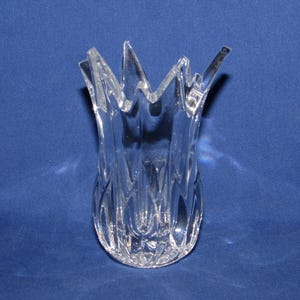 May include: A clear glass vase with a unique, spiky top. The vase has a tulip-like shape with a textured, patterned design on the lower portion. The vase is set against a solid blue background.