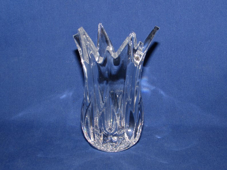 May include: A clear glass vase with a unique, spiky top. The vase has a tulip-like shape with a textured, patterned design on the lower portion. The vase is set against a solid blue background.