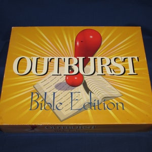 May include: A yellow box with the title "OUTBURST Bible Edition" in white text. The box art features a red exclamation mark and a book with radiating yellow lines. The box is on a dark blue surface.