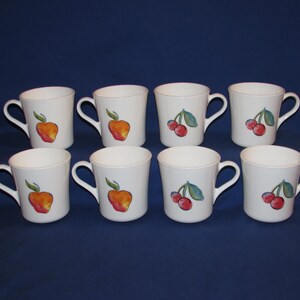 May include: Set of eight white ceramic mugs with a fruit design.  Four mugs feature a red and orange apple design and four mugs feature a red cherry design with green leaves.