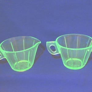 May include: A set of two vintage green glass creamer and sugar bowls. The bowls have a fluted design and are made of uranium glass, which glows under a black light.