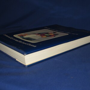 May include: A blue hardcover book with the title "The Collector's Encyclopedia of Dolls" and the author "Dolores Elizabeth and Richard Dennis". The cover features a colorful illustration of a doll holding a basket of fruit.