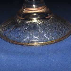May include: The base of a clear glass pedestal with a gold rim and a decorative etched pattern.