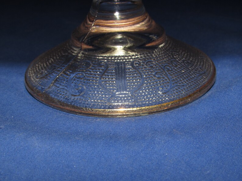 May include: The base of a clear glass pedestal with a gold rim and a decorative etched pattern.