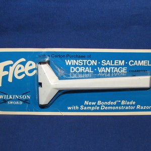 May include: A blue and white package with a white plastic razor and the text "Free with a Carton Purchase of Winston Salem Camel Doral Vantage Cigarettes".