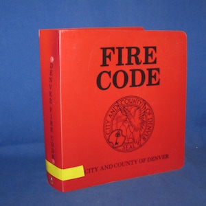 May include: A red binder with the text "FIRE CODE" in black lettering. The binder has a seal with the text "CITY AND COUNTY OF DENVER" on the front.
