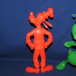 May include: Two plastic cartoon character figurines. One is red and is a caricature of a dog with a sailor hat. The other is green and is a caricature of a duck with a sailor hat.