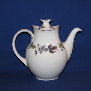 May include: White ceramic teapot with a lid and a vine design in shades of green, brown, and black. The teapot has a rounded body and a curved spout.