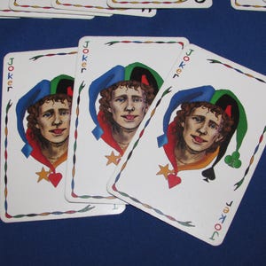 May include: Three playing cards featuring the Joker. Each card shows a portrait of a jester with a blue, green, and red hat. The cards have a white border with a decorative design and the word "Joker" in the corners.