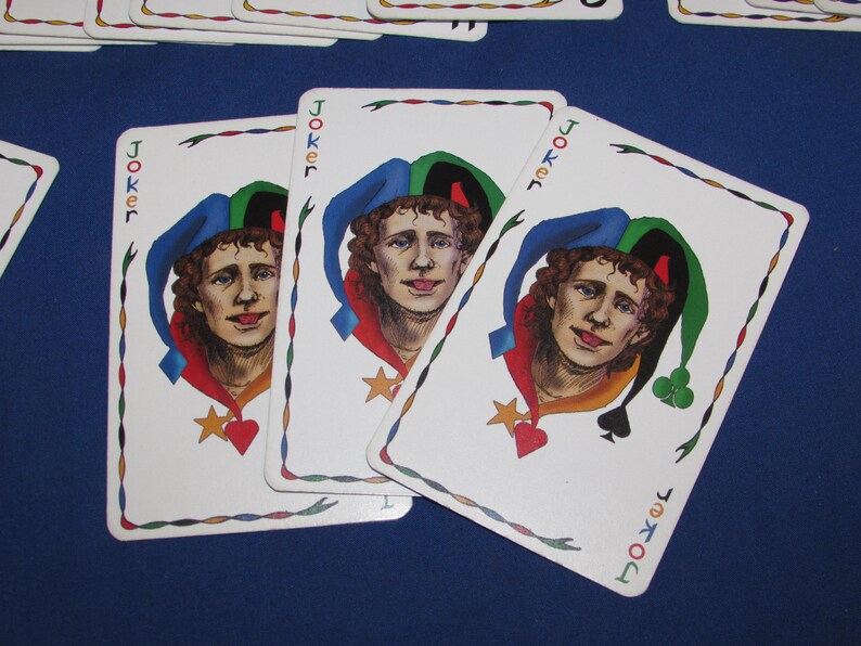 May include: Three playing cards featuring the Joker. Each card shows a portrait of a jester with a blue, green, and red hat. The cards have a white border with a decorative design and the word "Joker" in the corners.