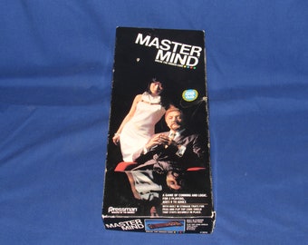 May include: A vintage board game box for Mastermind, a game of logic and deduction. The box features a black and white image of two people playing the game. The text on the box reads "Mastermind Break the Hidden Code".