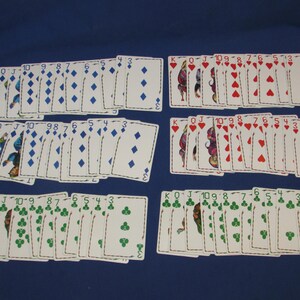 May include: Several decks of playing cards are arranged on a blue surface. The cards are organized into suits: diamonds, hearts, and clubs. Each card displays its suit symbol and number, with face cards also present.