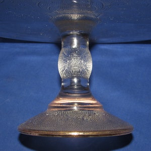 May include: A clear glass cake stand with a textured design and a gold rim. The stand has a round base and a single pedestal.
