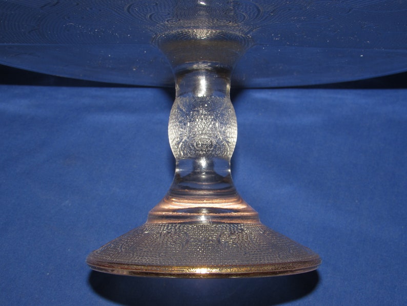 May include: A clear glass cake stand with a textured design and a gold rim. The stand has a round base and a single pedestal.