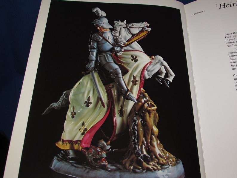 May include: A porcelain figurine of a knight on horseback slaying a dragon. The knight is wearing armor and a flowing cape, and the horse is white with gold accents. The dragon is green and has a chain around its neck.