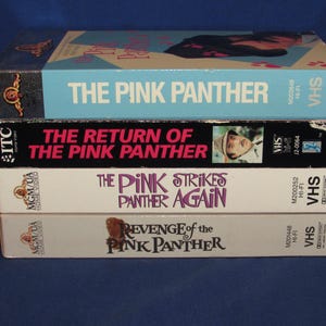 May include: A stack of four VHS tapes featuring "The Pink Panther" movie titles. The tapes are in various colors, including light blue, black, and white. The titles include "The Pink Panther," "The Return of the Pink Panther," and "Revenge of the Pink Panther."