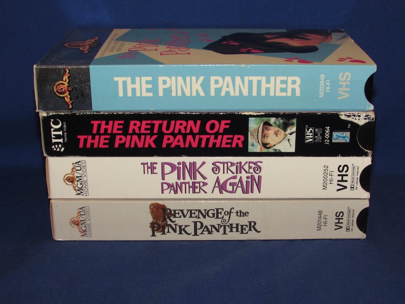 May include: A stack of four VHS tapes featuring "The Pink Panther" movie titles. The tapes are in various colors, including light blue, black, and white. The titles include "The Pink Panther," "The Return of the Pink Panther," and "Revenge of the Pink Panther."