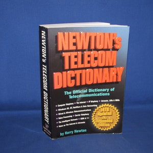 May include: A red and black book titled "Newton's Telecom Dictionary: The Official Dictionary of Telecommunications". The book is the 14th updated and expanded edition.