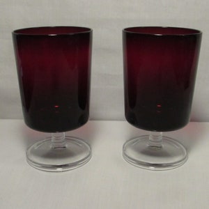 May include: Two stemmed drinking glasses with clear bases and dark red glass bodies.