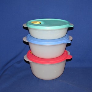 May include: Three clear plastic bowls stacked on top of each other, each with a different colored lid. The top lid is teal, the middle lid is blue, and the bottom lid is red. Each bowl has a handle on either side.