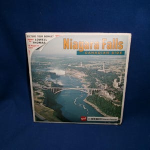 May include: A square View-Master picture tour booklet titled Niagara Falls Canadian Side, edited by Lowell Thomas. The cover features an aerial photograph of the Niagara River and bridge, with text indicating 16 pages in color and 21 stereo pictures.