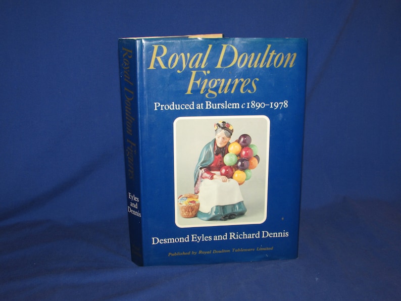 May include: A blue book titled "Royal Doulton Figures" with a picture of a woman holding a bunch of colorful balloons. The book was produced in Burslem, England from 1890 to 1978. The authors are Desmond Eyles and Richard Dennis.