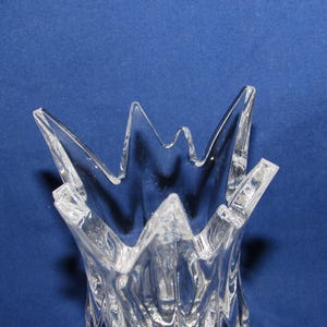 May include: Clear glass vase with a starburst design at the top. The vase has a textured surface and a flared, jagged rim. The background is a solid blue.