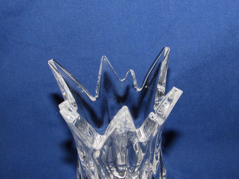 May include: Clear glass vase with a starburst design at the top. The vase has a textured surface and a flared, jagged rim. The background is a solid blue.