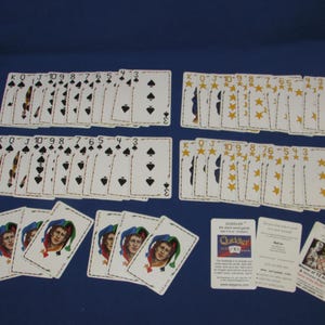 May include: A collection of playing cards, including two decks of spades, two decks of stars, and several joker cards. The cards are arranged on a blue surface, with the card suits and numbers clearly visible.