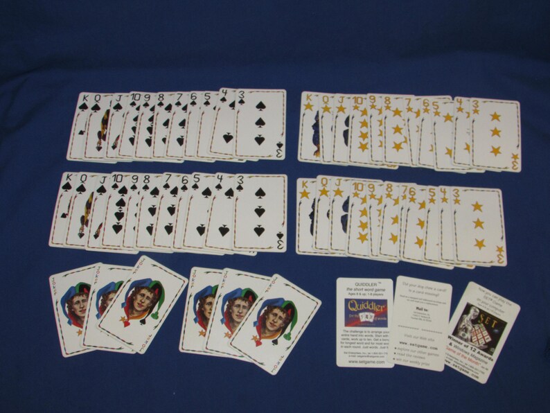 May include: A collection of playing cards, including two decks of spades, two decks of stars, and several joker cards. The cards are arranged on a blue surface, with the card suits and numbers clearly visible.