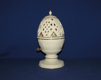 Puede incluir: Un candelero de porcelana blanca en forma de huevo con intrincados diseños con bordes dorados. El candelero presenta un delicado patrón calado y una base con un motivo floral.