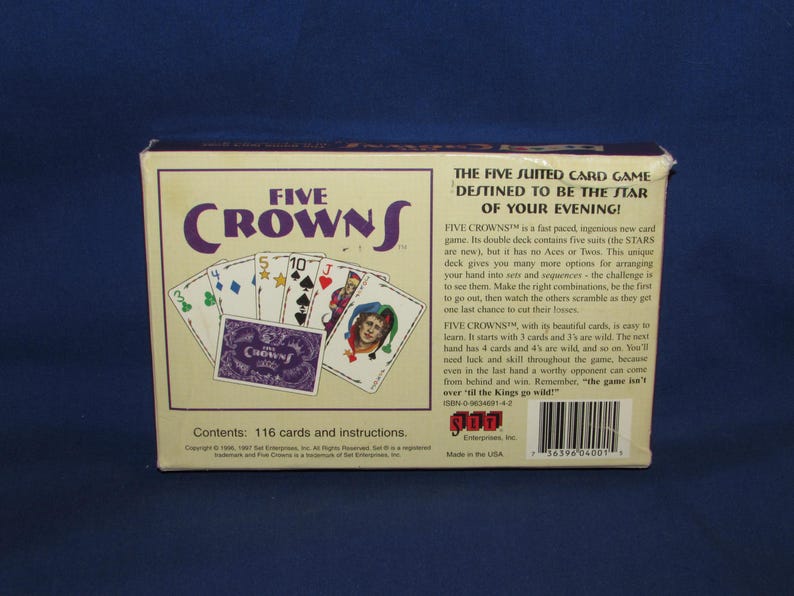 May include: A Five Crowns card game box with the game title in purple and white. The box displays playing cards with various suits and values. The text on the box reads "The Five Suited Card Game Destined to be the Star of Your Evening!"